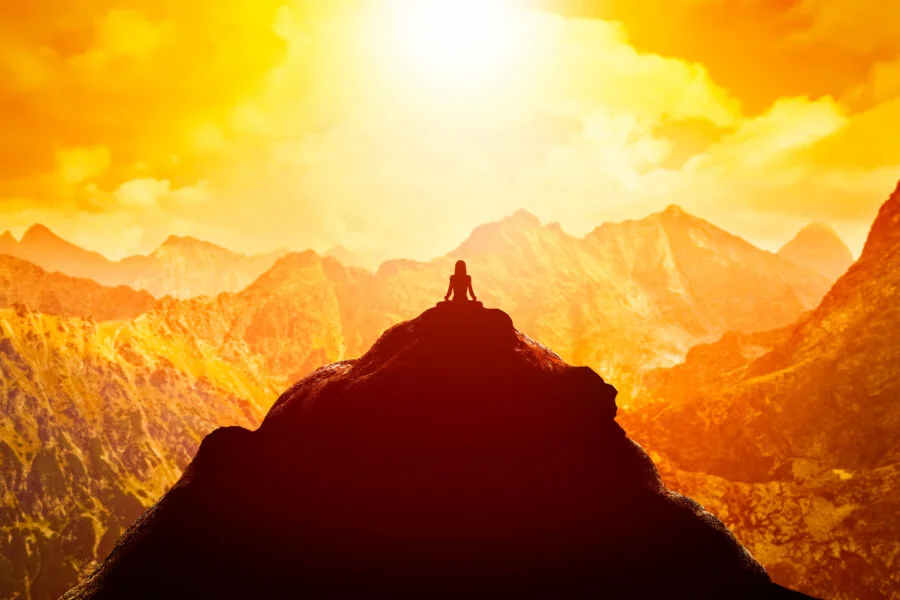 Woman meditating in sitting yoga position on the top of a mountains above clouds at sunset